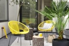 a small and bright modern terrace with yellow chairs, tree stump side tables and statement potted plants