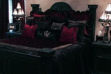 a sophisticated Gothic bedroom with neutral walls, carved wooden black furniture, crimson and black bedding and elegant lights