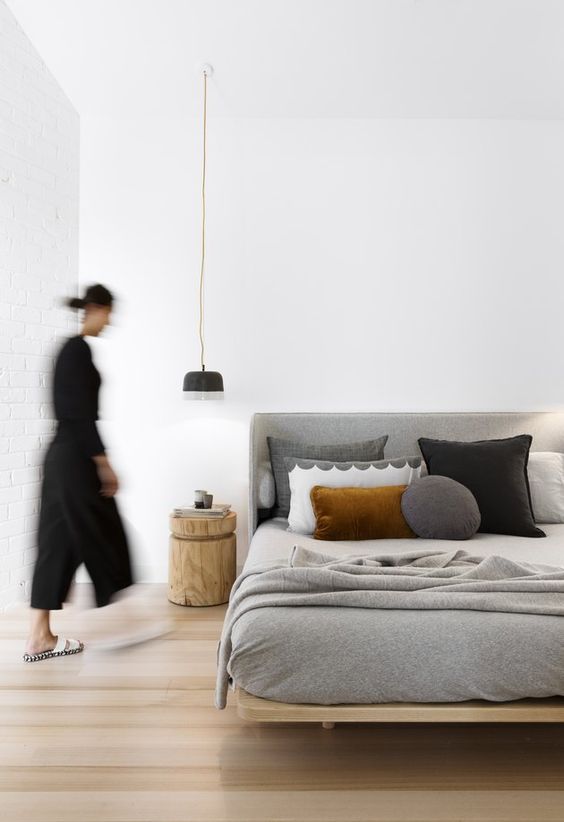 a stylish and neutral zen bedroom with a comfy wooden bed, grey and black bedding, a wooden nightstand and a pendant lamp