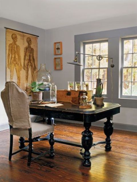 a vintage home office with a black carved desk, a vintage chair, potted plants, an industrial table lamp and a wooden box for storage