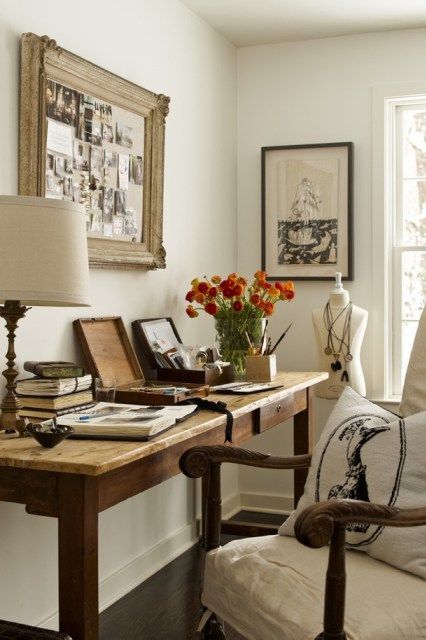 a vintage home office with a stained desk, a stained chair with neutral upholstery, some artwork and a vintage memo board