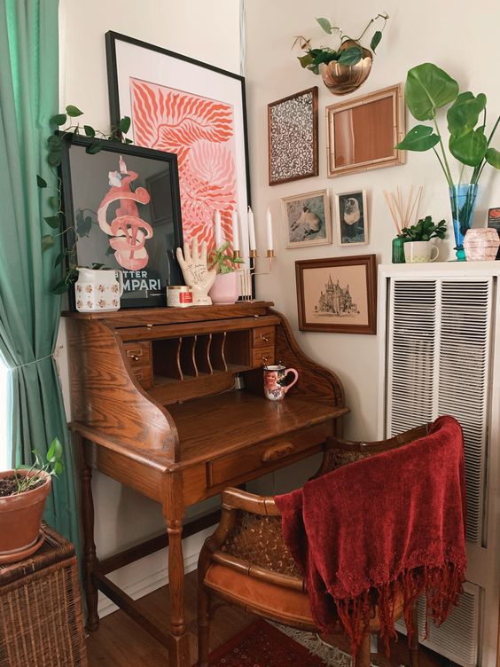 a vintage working nook with a gallery wall, a small stained bureau desk, a stained chair and some potted greenery