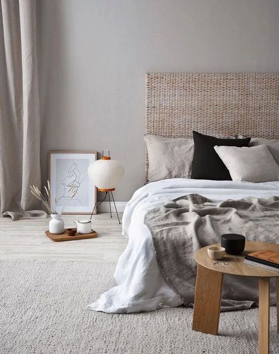 a zen-like bedroom in neutrals, with a woven headboard, neutral bedding, a low wooen table and some trays plus a floor lamp