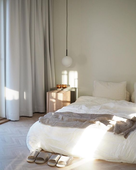 a zen-like bedroom with a bed right on the floor, a wooden nightstand, a pendant lamp and neutral bedding is chic