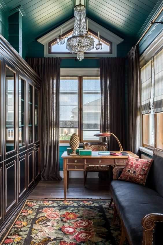 an elegant vintage home office with black bookcases, a stained desk, a floral chair and a rug, a blue sofa and a jaw-dropping crystal chandelier