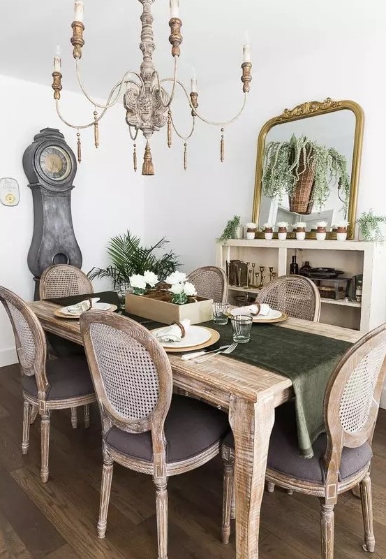 a French country chic dining room with a credenza, a large mirror, lots of greenery and an elegant stained dining set plus a vintage chandelier