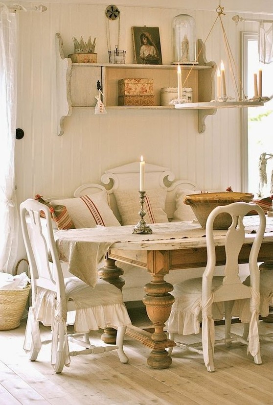 a French country chic dining room with neutral vintage furniture, a large stained vintage table, a wall-mounted shelf and a simple chandelier
