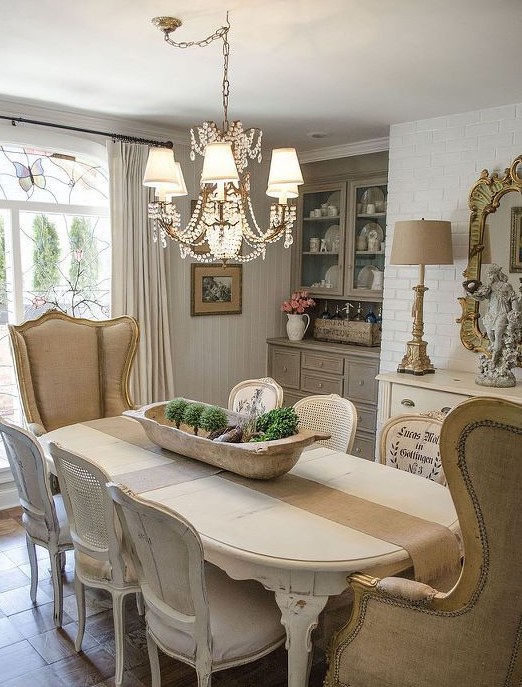 a French country dining room with a built-in taupe storage unit, a neutral sideboard, an oval table and white chairs and wingback chairs