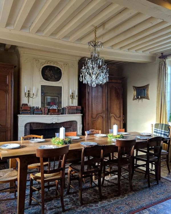 a French country dining space with a non-working fireplace, a long stained table and mismatching chairs, a crystal chandelier