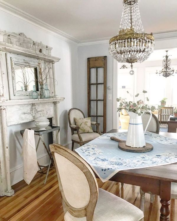 a French farmhouse dining room with a faux fireplace, a stained table, vintage chairs and a crystal chandelier