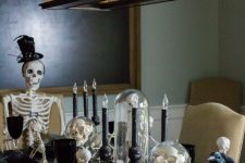 a Halloween table setting with black plates, goblets and candles, skulls and skeletons, white pumpkins