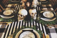 a Halloween tablescape with black and white linens, gold cutlery, skulls, candles and printed plates plus greenery