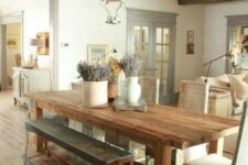a Provence dining room with a wooden floor and ceiling with beams, a stained table, benches and woven chairs, a cool pendant lantern