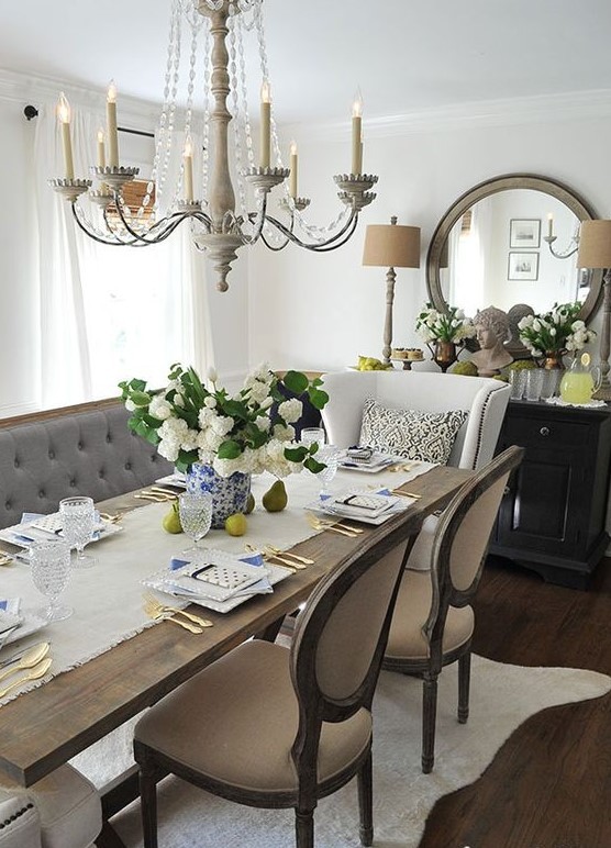 a beautiful French cream-colored dining room with off-white and beige furniture with a vintage loveseat, chairs, a beautiful chandelier and a round mirror