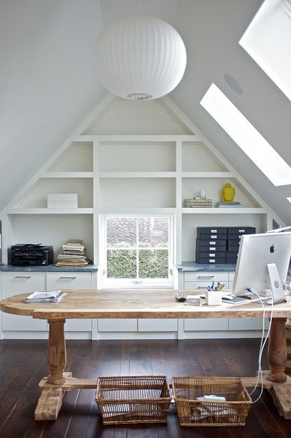 a beautiful attic home office with skylights, a built-in shelving unit, a large stained desk, baskets and a sphere pendant lamp