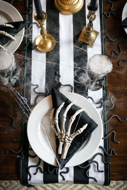 a black and white Halloween table with a striped table runner, black napkins, skeleton hands, gold candleholders and snakes