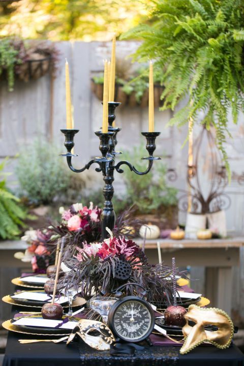 a bold and refined Halloween tablescape with gold cutlery and chargers, masks, deep toned blooms and feathers and candles