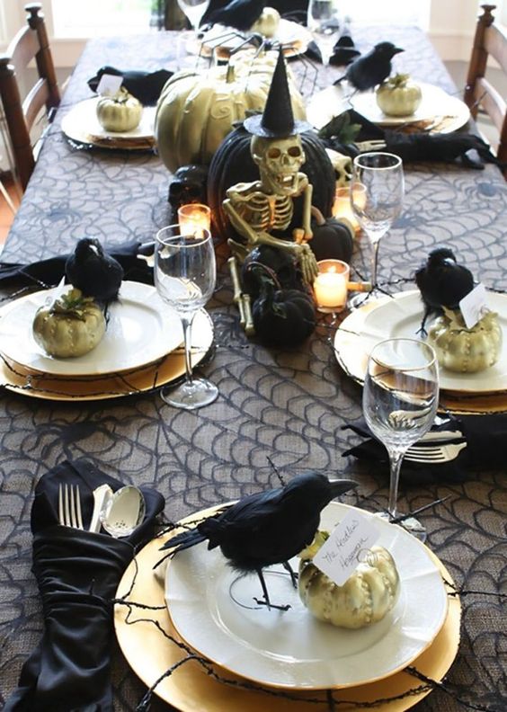 a chic Halloween tablescape with a spiderweb tablecloth, black napkins, black crows and pumpkins, candles and twigs plus a skeleton