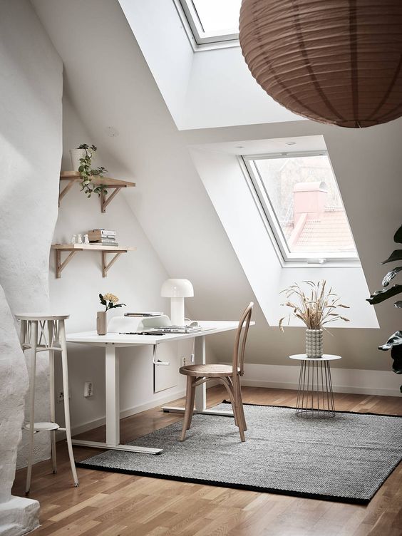 a chic attic home office with a white desk and neutral chair, some shelves, a tall stool and some dried blooms on a stand