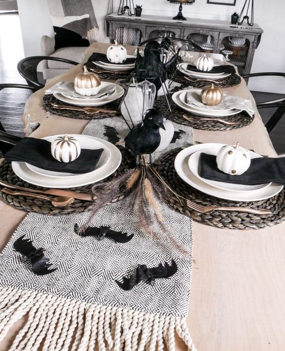 a chic black and white Halloween tablescape with black crows, bats, napkins, painted pumpkins, woven placemats and wheat
