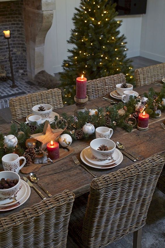 a chic winter table setting with an evergreen, lights and pinecones runner plus wooden stars and ornaments, pillar candles and pinecones in bowls