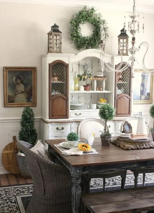 a classic farmhouse dining space with a shabby chic dining set, wicker chairs, a white and brown buffet and beautiful artworks