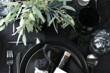 a classy modern Halloween tablescape with all things black, skulls, candies, eucalyptus, candles and matte cutlery