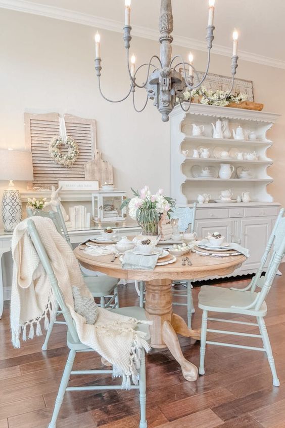 a cozy French cottage dining room with a white buffet, a console table, a stained table, mint blue chairs and a whitewashed chandelier