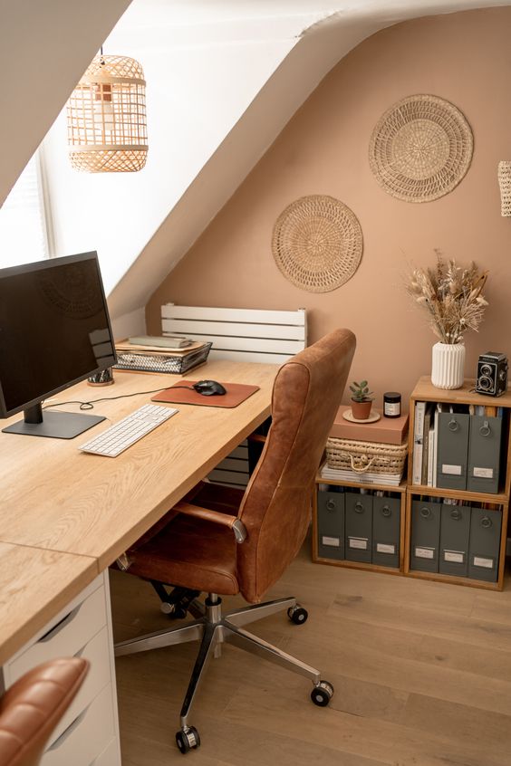 a cozy warm-colored home office with a comfy desk, an upholstered chair, bookshelves, decorative plates, a pendant woven lamp