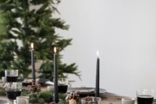 a cozy winter table with an evergreen, pinecone and nut runner, black candles and black plates plus gingerbread cookies over the table