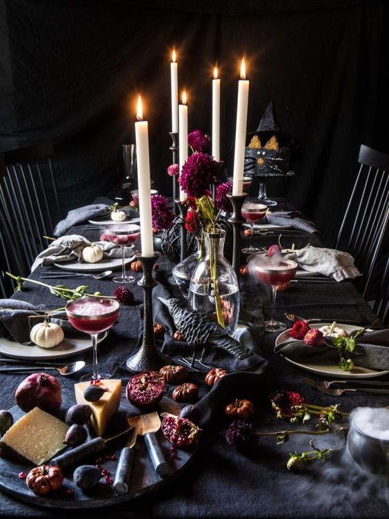 a decadent Halloween tablescape with black linens, crows, bold purple blooms, candles and dried flowers