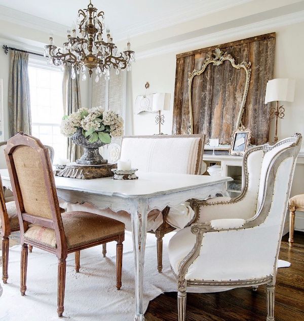 a fab neutral dining room with a vintage refined dining table, stained and white chairs, a crystal chandelier and a rustic artwork