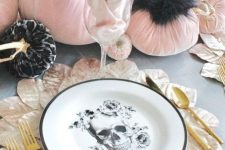 a glam Halloween table setting with black and pink velvet pumpkins, a skull plate, gold cutlery and leafy placemats
