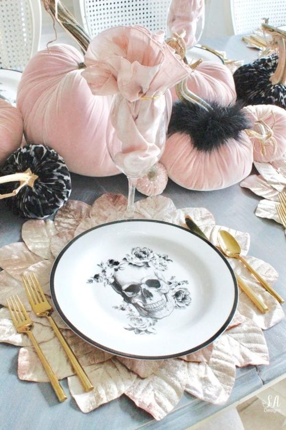 a glam Halloween table setting with black and pink velvet pumpkins, a skull plate, gold cutlery and leafy placemats