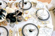 a glam Halloween tablescape with white and black pumpkins, black feathers, candles, gold cutlery and black chargers