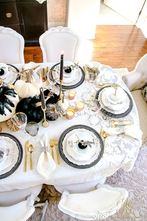 a glam Halloween tablescape with white and black pumpkins, black feathers, candles, gold cutlery and black chargers