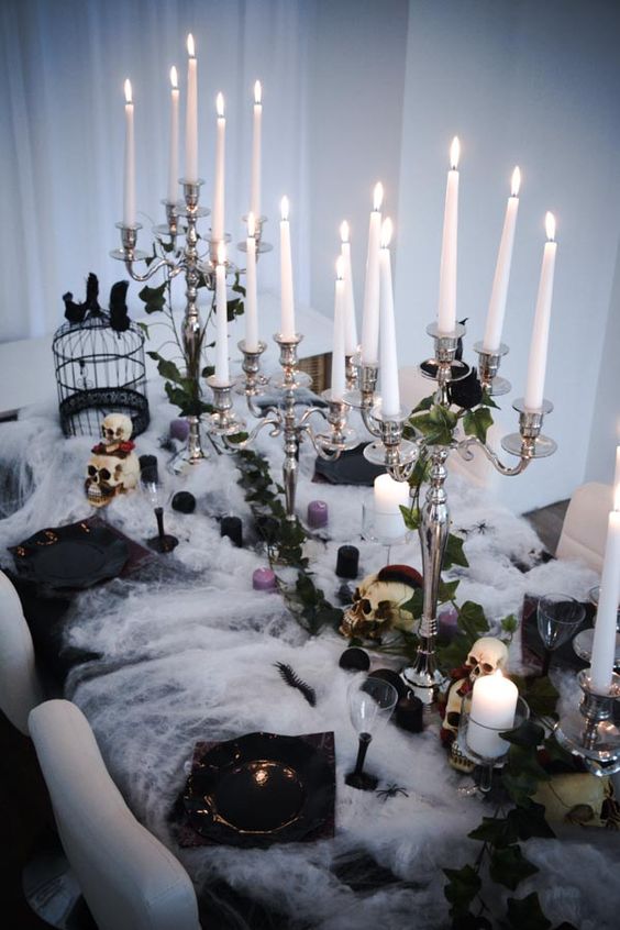 a gorgeous Halloween tablescape with black, purple and white candles, greenery, roses, black porcelain, crows and skulls