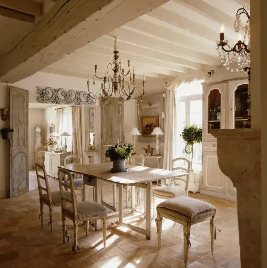 a light-filled French dining room with a chic buffet, a console table, a dining table and white chairs, crystal chandeliers and greenery