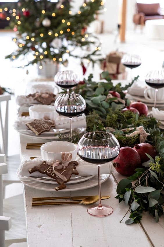 a lush winter tablescape with a greenery runner with pomegranates, gingerbread bcookies and elegant cutlery