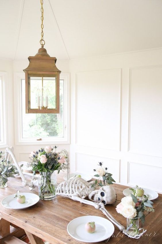 a modern Halloween tablescape with a skeleton, neutral blooms and greenery, fruit and white porcelain