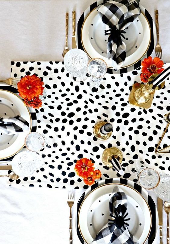a modern glam Halloween tablescape with a Dolmatin runner, printed plates, brigth blooms, gold candleholders and black spiders