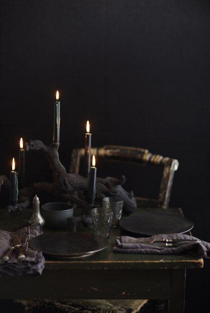 a moody black Halloween tablescape with black candles, plates, napkins, glasses and bowls is very chic