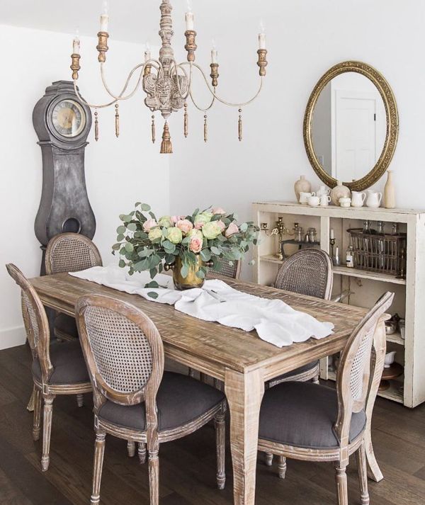 a neutral French chic dining room with a storage cabinet, a mirror, a stained vintage table, vintage chairs and a grandfather's clock