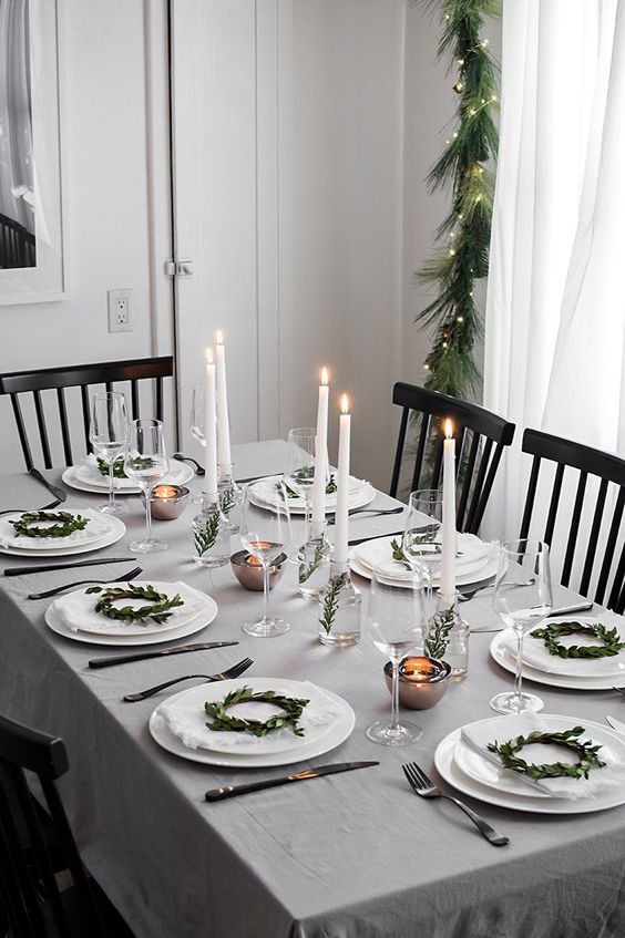 a neutral and simple winter tablescape with mini greenery wreaths for decor, candles in vases with greenery and mini tealights