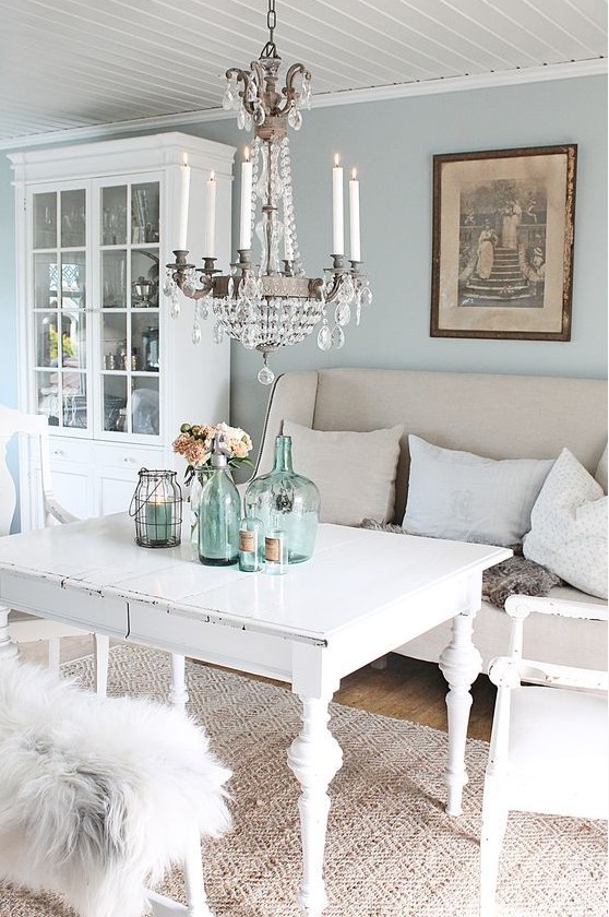 a pastel shabby chic dining room with blue walls, white shabby chic furniture,a crystal chandelier, blue bottles and jars