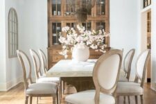 a refined French dining space with a stained glass buffet, a large table with a stone tabletop, neutral chairs and a cool chandelier
