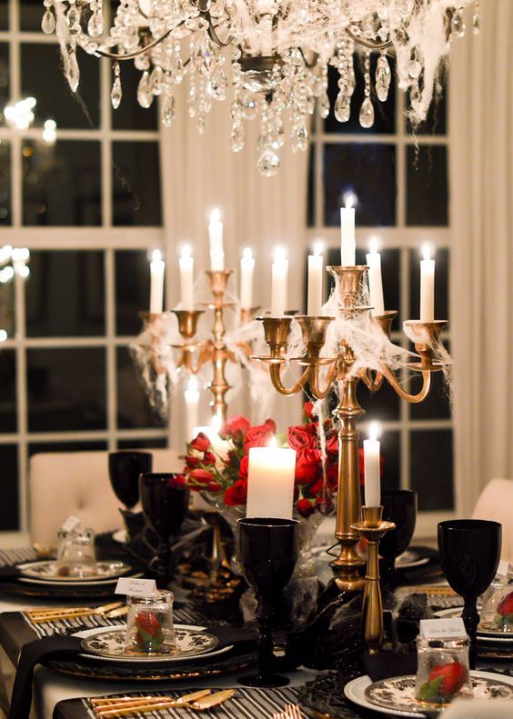 a refined Gothic tablescape with candles covered with spiderwebs, red roses, black goblets and plates, gold cutlery and candleholders