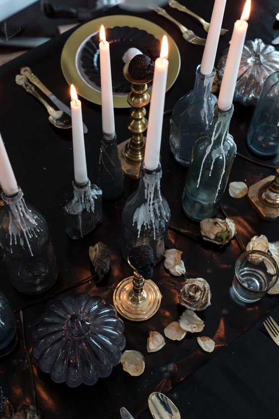 a refined Halloween tablescape with candles, dried petals, black pumpkins and touches of gold here and there