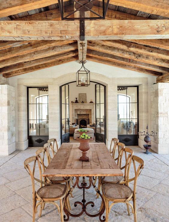 a rustic French dining room with a stone floor and walls, a wooden ceiling with beams, a stained table and vintage cane chairs