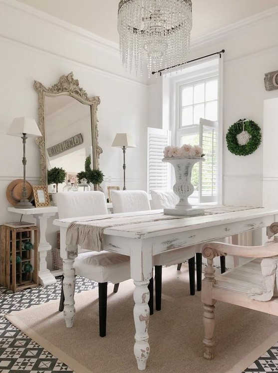 a shabby chic dining space with neutral and pastel furniture, blooms and greenery, a statement crystal chandelier and a refined mirror